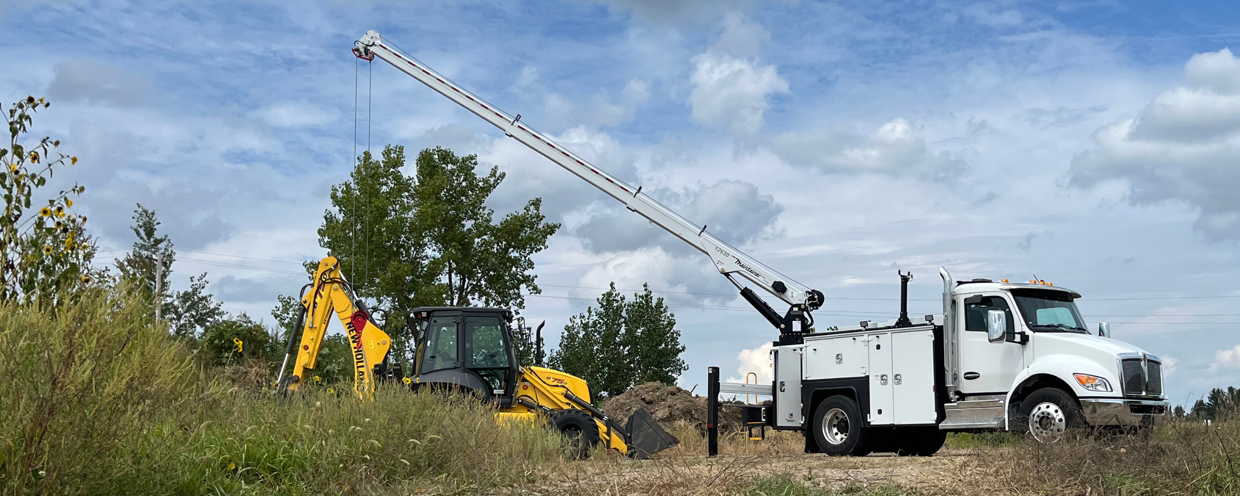 White utility truck with extended crane in a field with construction equipment.
