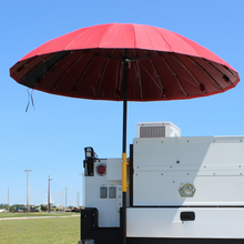 A large red canopy-style umbrella mounted on a black pole attached to the back of a white utility vehicle, photographed outdoors under a clear blue sky.